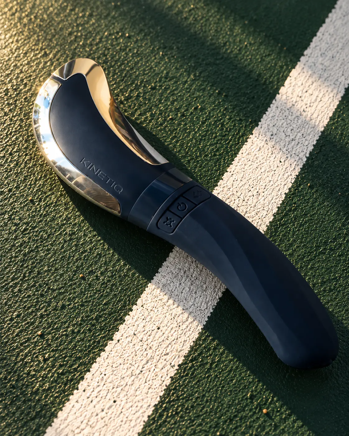Heated muscle scraping tool resting on the white line of a green outdoor court